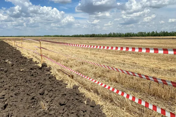 stock image A restrictive plastic tape separates the treated and untreated fields. Financial problems of farmers and judicial restrictions.