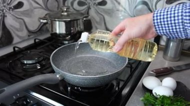 Bir adam, mutfağındaki gaz sobasında çubuksuz bir tavada omlet pişiriyor. Kızartma tavasına daha iyi pişirmek için ayçiçeği yağı dökülür..