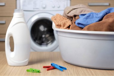 Kirli çamaşırlarla dolu bir sepetin ve plastik bir şişe sıvı jelin yakın çekimi. Renkli kumaşlar için modern temizlik ürünleri, bir çamaşır makinesinin arka planına karşı.