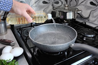 Kızartma tavasına daha iyi pişirmek için ayçiçeği yağı dökülür. Bir adam, mutfağındaki gaz sobasında çubuksuz bir tavada omlet pişiriyor..