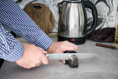 Bir adam mutfak mutfağında mutfak bıçağını biler. Ahşap bir arka planda kesim tahtası ve mutfak aletleri.