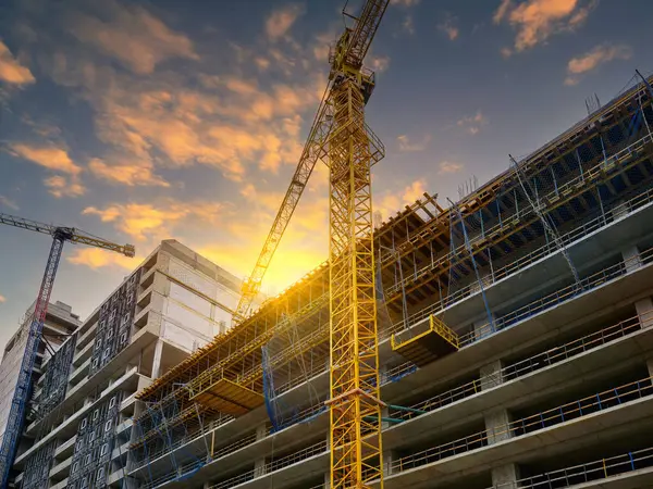 Yeni bir konut kompleksi inşaatı. Güzel bir günbatımı gökyüzünün arka planına karşı iki gökdelenli vinç.
