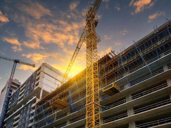 Строительство нового жилого комплекса. Два высотных крана на фоне прекрасного закатного неба.