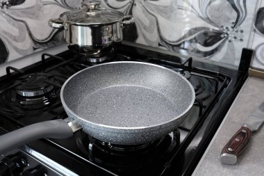 Boş kızartma tavası, mutfak arka planındaki gaz sobasının üzerinde duruyor. Yemek hazırlığı.
