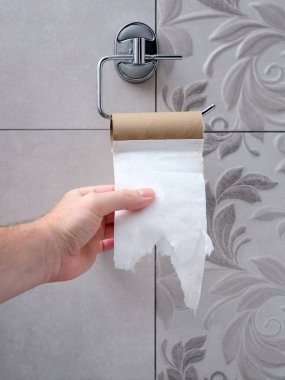 Bir adamın eli boş bir tuvalet kağıdı tutacağına uzanıyor. Kağıt sıkıntısı. Dikey resim.