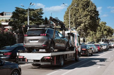 Bir araba çekicisi tamir istasyonuna bir SUV ile gider. Şehirde yoğun trafik var..