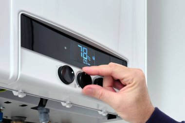 Bir adam evdeki modern bir dijital gaz kazanının ısısını ayarlar. Dijital gösterge ile ayarlanıyor. 