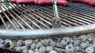 Bir adam açık ızgarada farklı etlerle büyük sosisler pişiriyor. Domuz eti, tavuk, sığır sosisi. Büyük bir grup insan için lezzetli yiyecekler..