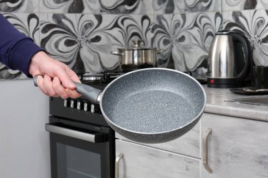 Ev mutfağının arka planında elinde boş kızartma tavası tutan adam. Evde yemek pişirmek için modern yemek takımı.