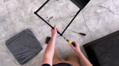 Orta yaşlı bir adam manuel tornavidayla bir sandalyeyi bir odada birleştirir..