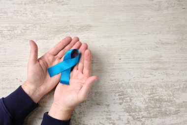 Erkek ellerinin soyut ahşap arka planda mavi kurdele uluslararası sembolü tutarken yakın plan. Kavramsal imaj zamanında tedavi ve hastalıkların önlenmesi. Seçici odak.