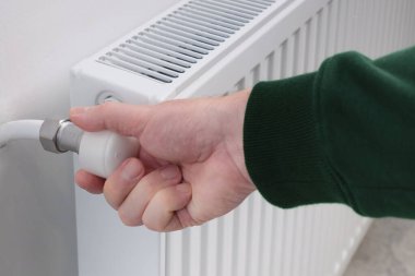 Adamın biri, bir apartmanda ya da evde ısıtma radyatörünün vanasını açıyor. Soğuk mevsimin başlangıcı. Elle radyatörü açıp kapatma.