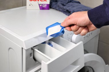 Çamaşır makinesine beyaz çamaşır tozu döken bir adamın yakın çekimi. Renkli ve beyaz kıyafetler için modern temizlik ürünleri.