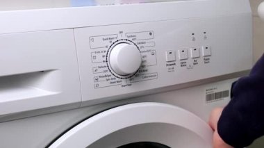 Çamaşır makinesinin panelindeki çamaşır modunu seçmek için bir adamın el dönüşü çemberi seçici.