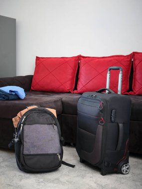 Tekerlekli modern bavul ve kanepenin yanındaki oturma odasında sırt çantası. Seyahatten ya da iş gezisinden önce bir şeyler paketlemek. Dikey resim.