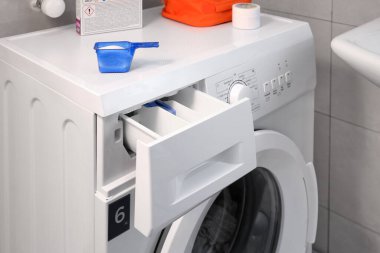 Çamaşır odasında çamaşır makinesinde bulaşık yıkamak için açık bir konteynır. Renkli ve beyaz kıyafetler için modern temizlik ürünleri.