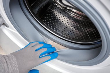 Çamaşır makinesinin lastiğindeki kiri kontrol ediyor. Çamaşır makinesinde küflü, kirli lastik conta yakın plan. Çamaşır makinesi bakımı.