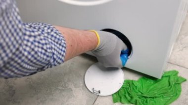 Eldivenli servis teknisyeni çamaşır makinesinin kirini kontrol ediyor..