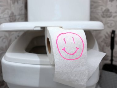 Üzerinde komik bir gülen surat çizilmiş tuvalet kağıdı rulosu dairenin banyosunun tuvalet kapağında duruyor. Hassas bağırsak ve sindirim sorununun kavramsal görüntüsü.