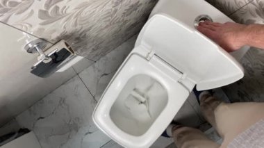 Tuvaletteki sifon düğmesine basan adamın üst görünümü.