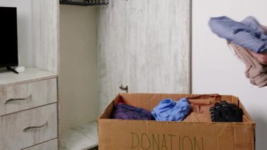 Adamın biri eski kıyafetleri bağış kutusuna koyuyor. Arka planda boş bir elbise dolabı var..