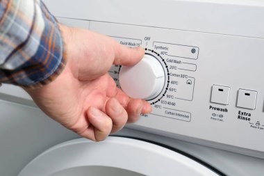 Bir adamın eli çamaşır makinesi panelinin çamaşır yıkama modu sıcaklık düğmesini ayarlar. Kirli çamaşırları yıkamaya hazırlanıyorum..