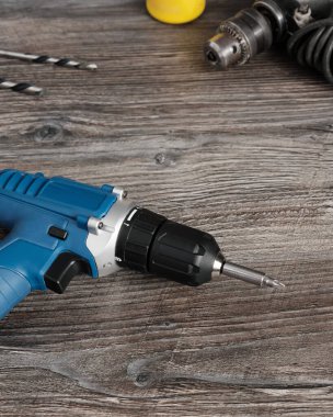 Tahta bir masanın üzerinde bir el tornavida ve elektrikli matkap var. İnşaat ve onarım için modern çalışma araçları. Dikey resim.