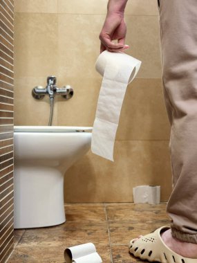 Bir adam tuvaletteki tuvaletin önünde tuvalet kağıdı tutuyor. Bağırsak sağlık sorunları ve ishal..