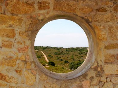 Korsika 'nın kuzeybatısındaki Calvi kasabasına hakim olan Chapelle de la Serra' nın surlarında açılan yuvarlak taştan bir pencereden Balagne manzarası..