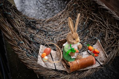 Bayramlık kıyafetlerle süslenmiş bir Paskalya tavşanı heykeli renkli yumurta ve havuçların yanında hasır bir sepette duruyor.. 