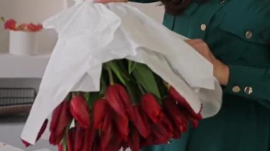 Beyaz kadın çiçekçi, bereketli bir buket lale topluyor. Bir profesyonel taze bir buket yapar. Küçük bir iş. Bir kadın kâğıt krep buruşturup içine bir buket lale sarar.