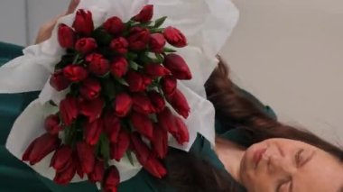 Beyaz kadın çiçekçi, bereketli bir buket lale topluyor. Bir profesyonel taze bir buket yapar. Küçük bir iş. Bir kadın kağıt krep buruşturup içine bir buket lale sarar. Dikey video.