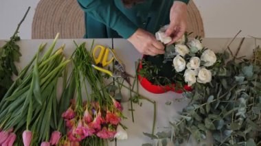 Beyaz kadın çiçekçi güzel bir çiçek aranjmanı hazırlıyor. Yukarıdan bak. Kadın çiçekleri budayarak keser ve kalp şeklinde bir çiçek aranjmanına koyar..