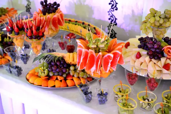 Buffet, fruit mix. Portioned fruits are in abundance on the table. Grapes, grapefruit, melon, orange, raspberry, kiwi, blueberry.