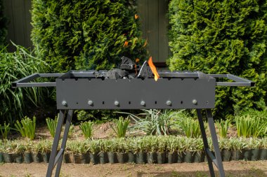 Gri ızgara. İçinde kömür var. Izgarayı et kızartmaya hazırlıyorum. Dışarıda, evin arka bahçesinde. Çevresi yeşilliklerle çevrili. Yakın çekim..