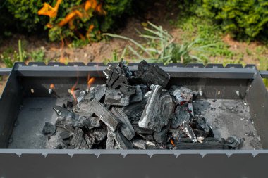 Gri ızgara. İçinde kömür var. Izgarayı et kızartmaya hazırlıyorum. Dışarıda, evin arka bahçesinde. Çevresi yeşilliklerle çevrili. Yakın çekim..