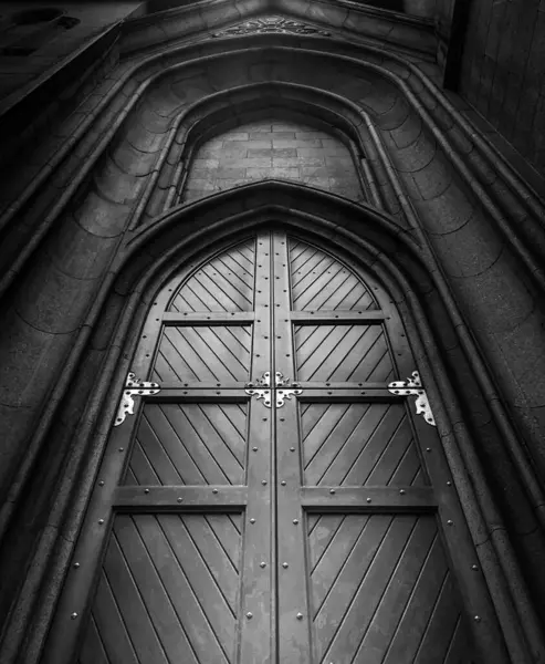 Porta de madeira em arco gtico da Catedral da S, em So Paulo. Fotografia em preto e branco com ngulo dramtico que valoriza os detales arquitetnicos and a imponncia da construo histrica.