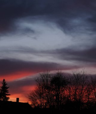 Burning clouds - red blue navy blue sky, house and trees in the background. Dark sky concept