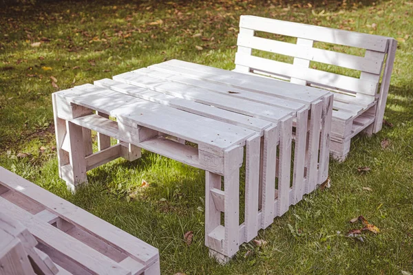 White garden pallet furniture in the autumn sun, leaves and a little bee on the bench
