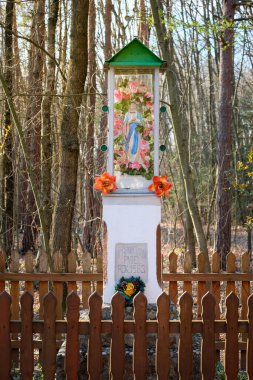 Ormanda bir yol kenarı şapeli, tespihi ve çiçekleri olan bir Maria, her yerde çiçekler, Polska kapliczka