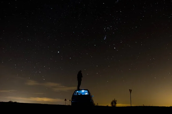 A man standing on a car in the background of stars with a night sky, a shining galaxy