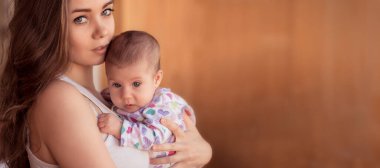 Genç anne evde bebeğini nazikçe kucağında tutuyor, hassas aile bağı anı..