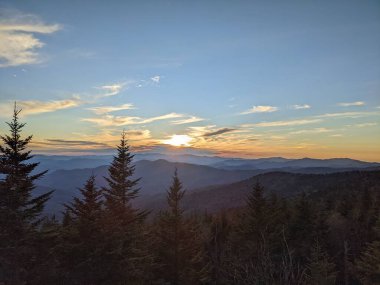 Sun setting behind mountains with trees in foreground 
