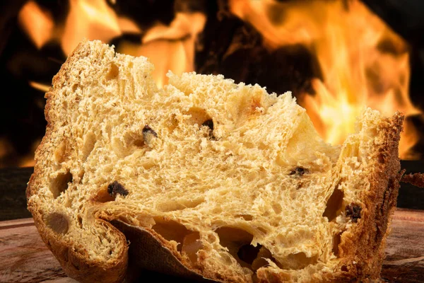 stock image Sliced panettone on wood with blurred fire background.