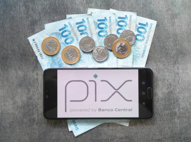 Bahia, Brezilya, 02 Haziran 2023. Brezilya parasının para ve banknotları üzerinde akıllı telefon ekranında Pix uygulaması.