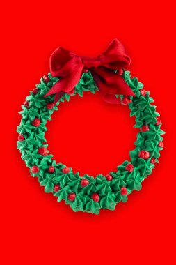 Kırmızı arka planda kırmızı fiyonklu Noel çelengi.