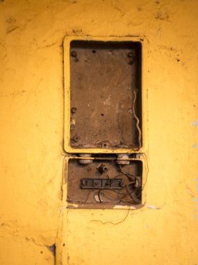 Sarı duvardaki kırık elektrik kutusu..