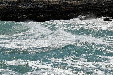 Dalgalar dalgalar dalgalı yeşil-mavi deniz ile kayalık kıyı şeridinde