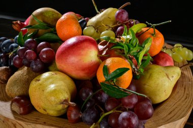 Büyük bir ahşap kaseye yerleştirilmiş sonbahar meyvelerinin yakın çekimi.