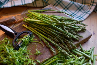 Wild asparagus on a wooden cutting board to be cooked, with nearby knife and tool to peel the stems clipart